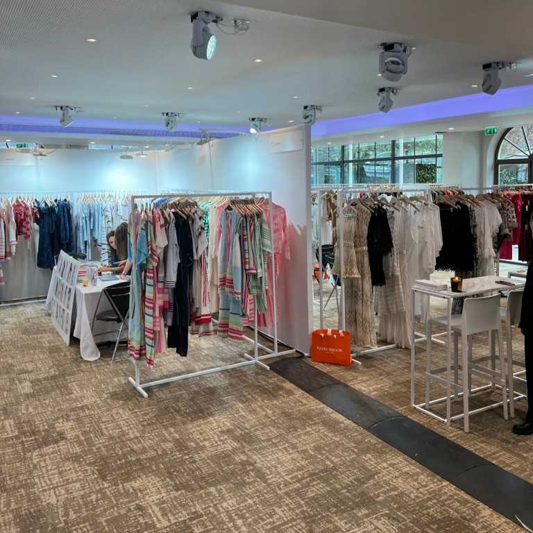 Clothing store interior with racks of colorful garments, a table with seated person working, and bright, airy lighting creating a calm atmosphere.