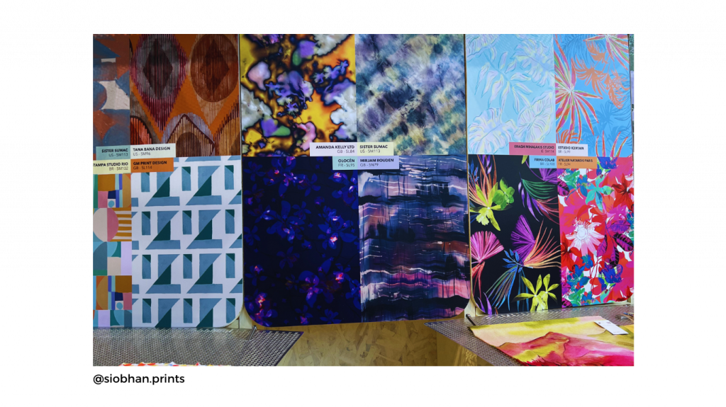 A colorful display of fabric swatches featuring various abstract and floral patterns in vibrant blues, pinks, and oranges for textiles and surface design. Labels with designer names are visible.